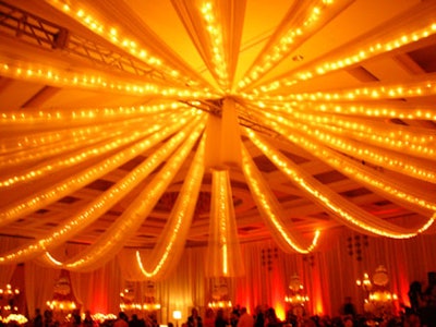 The ceiling was draped from corner to corner with long white linen panels lit with piping of white lights and converging in the center of the room to create a maypole overhead.