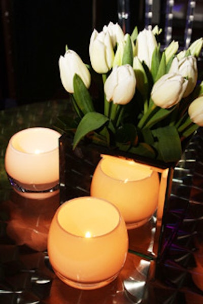 Mirrored glass vases filled with tulips, surrounded by white candleholders, topped 10 cocktail tables in front of the stage.