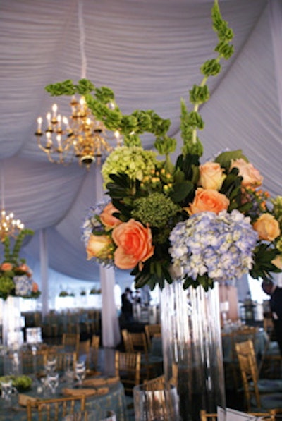 Florists created a vignette of clear glass cylinders with an array of vibrant blue hydrangeas and golden peach roses cascading from each vase as a high-profile centerpiece.