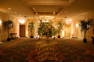 An oversize floral arrangement—featuring orchids, leaves sprayed with gold paint, and long twigs—topped a cocktail table draped in green and gold fabric in the reception space.