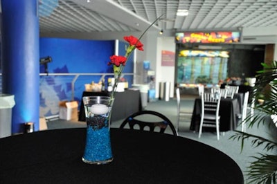 Cocktail tables were topped with simple centerpieces made from narrow glass vases filled with turquoise and black aquarium stones and two red carnations for a splash of color.