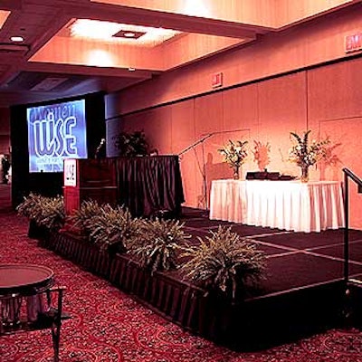 A fern-lined stage area was set on one side of the room with video monitors on both sides and a podium in the middle.