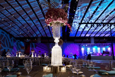 Kehoe Designs topped tables with elevated crystal vases that sprouted clusters of pale purple roses accented with silver palm leaves.