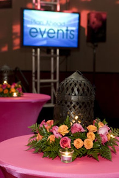 Each of the high tables outfitted in pink spandex covers was topped with a small birdcage surrounded by a pink and orange rose floral arrangement provided by Temporary Tropics.