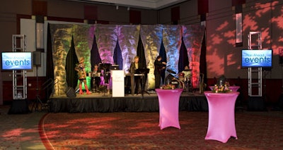 Creative Show Services created a stage backdrop of black pipe and drape with screening material and creative lighting.