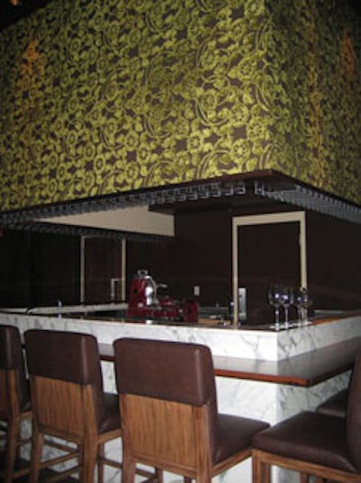 The restaurant's 15-seat elevated dining bar, topped with a green-patterned hanging structure, includes a separate charcuterie and cheese menu.