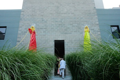 An installation featuring two colorfully dressed women on stilts controlling shirtless men with string stood at the main entrance.