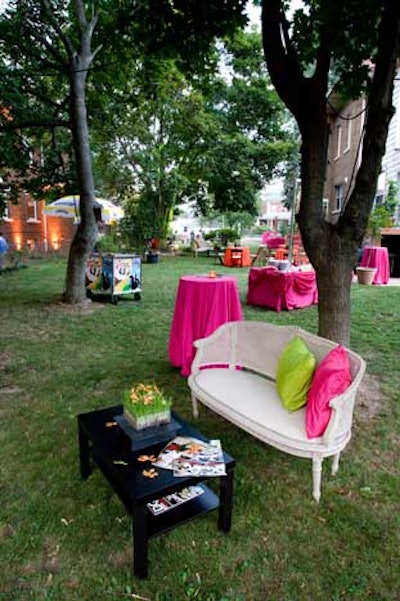 Bright pink and green pillows jazzed up white patio furniture set in front of black coffee tables on the lawn.