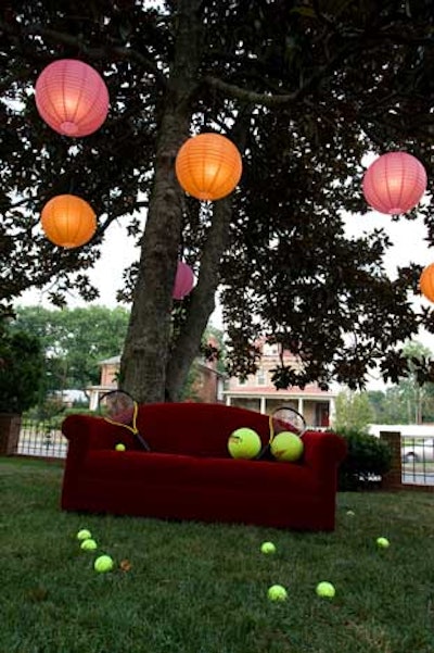 Colorful paper lanterns hung above a large red velvet couch covered with oversize tennis balls and rackets for guests to pose beside for pictures.