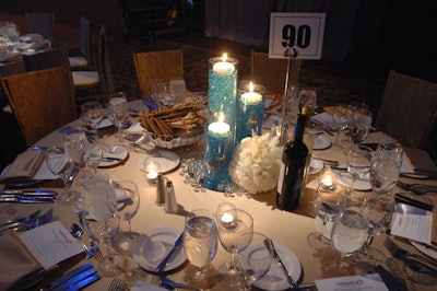 Table settings included glass cylinders with blue beads and gold Chiavari chairs dressed with crushed satin runners.