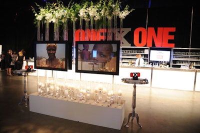 Silent auction items sat in front of tall glass tubes lit by candles and filled with white floral arrangements at the OneXOne gala.