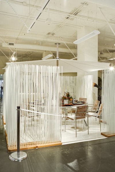 Tall white stems surrounded Janus et Cie's creation, which channeled an outdoor feel with patio-like seats and an umbrella that hovered over the table.