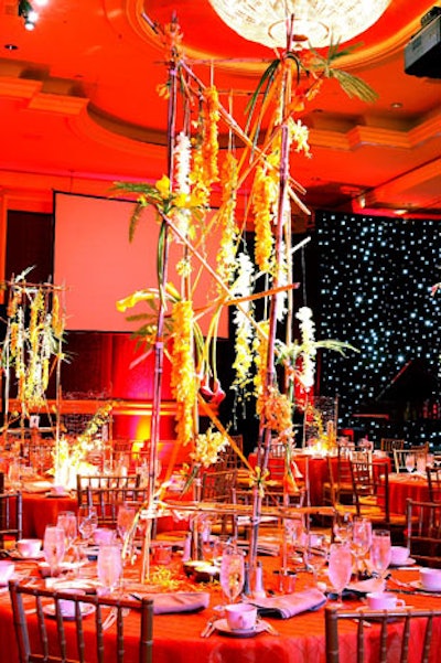 En Masse hung yellow, orange, and white orchids and calla lilies from six-foot-tall bamboo armatures to compliment the fiery orange silk tablecloths.