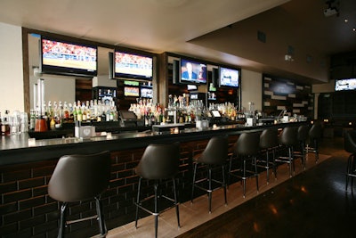 At the front of the space sits the main bar, which is furnished with high-back stools, mirrors, and several TVs.