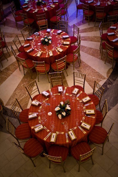 Tables with muted red linens and red, white, and green centerpieces dotted the pink-hued marble floor.