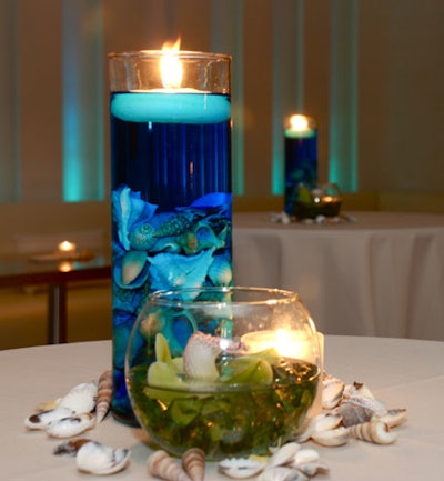 A glass pillar container and small fishbowl, filled with seashells, blue and green water, and a floating candle, topped the cocktail tables.