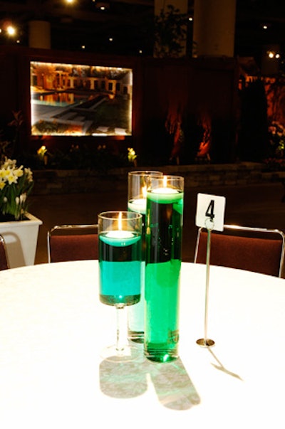 Glass vases filled with varying shades of green water and floating candles topped tables in the sponsor pavilion.