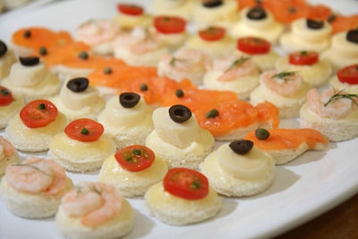 A crew of kitchen workers assembled canapes topped with shrimp, tomato, heart of palm, and smoked salmon.