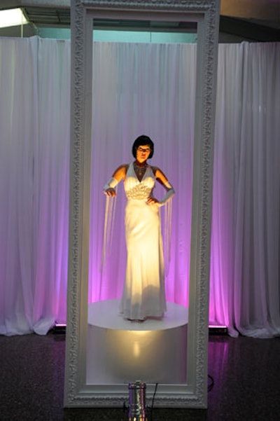 Three models wearing long gowns, pearls, and elbow gloves posed on pedestals placed behind oversize white frames during the cocktail reception.