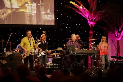 Brian Wilson performed on a stage set with a starry backdrop, palm trees, and sunset hues.