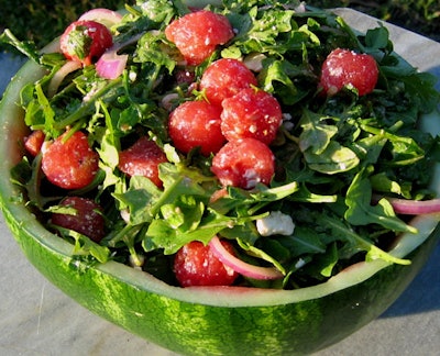 An arugula, watermelon, red onion, and feta cheese salad served in a carved-out watermelon.