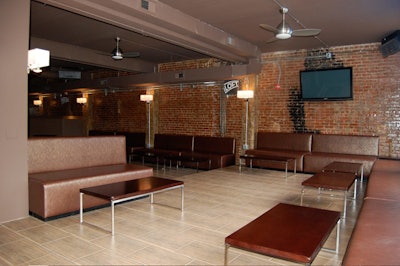 The front of the lounge has a stage area as well as brown faux-leather seating and cocktail tables.