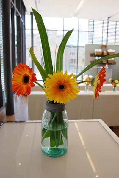 Glass jars filled with orange and yellow gerbera daisies topped tables throughout the space.