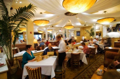 The main dining room on the first floor is decorated with painted gold walls, rich burgundy and brown upholstered chairs and banquettes, and white draping on the ceiling.