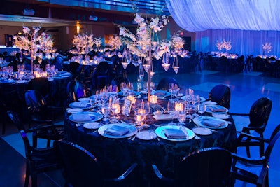 Damask linens from Around the Table topped tables surrounded by black Louis Ghost chairs in the blue-lit dining room.