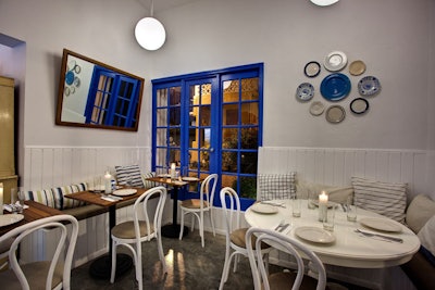 The primarily white restaurant is accented with bright blues, striped pillows, and vintage plates on the wall.