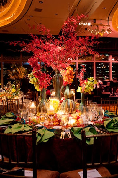 A centerpiece of orchids in chunky blue and green vases served as a centerpiece at Rinfret Ltd. and Glorimundi Floral's table. Surrounding the vases were small, low arrangements of flowers, candles, and peacock feathers.
