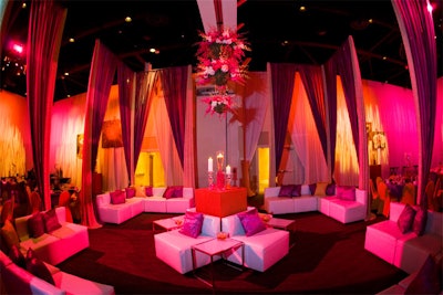 ConceptBAIT created a lounge area with white leather sofas, plum and sparkling gold drapes, and a floral chandelier.