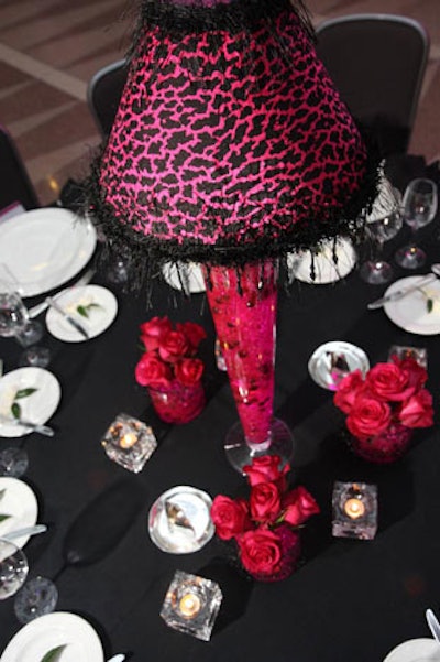 A fluted, pink-lit centerpiece with a feather-trimmed black and leopard print shade topped each table.