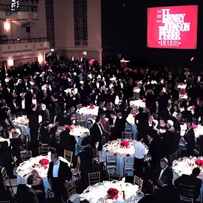 During dinner in the grand ballroom, tables had red rose centerpieces, and a large screen showed the event's logo and broadcast the proceedings.