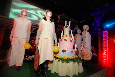 During the birthday opera, performers crowded around a layered prop cake.