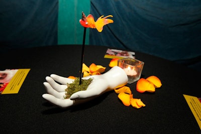On highboy tables, abstract centerpieces combined white hands, bits of moss, and plastic goldfish wearing tiny party hats.