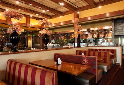The main dining room is decorated with dark red and gold printed banquettes and light wood accents.