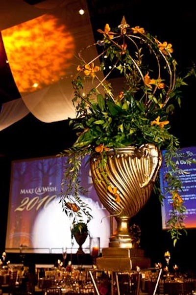 Tables got one of three centerpiece designs. In one arrangement, a metal riser held a ram urn, which was topped with a gold wire topiary. Ivy and orange orchids filled the urn.