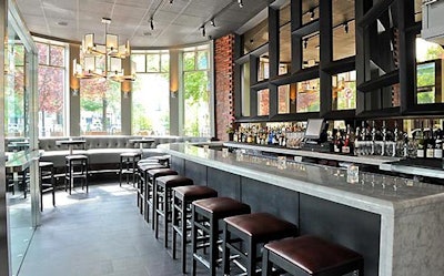 Near the bar is a lounge area with cocktail tables and seating along bay windows overlooking Commonwealth Avenue.