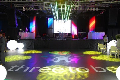 The Three to Be logo marked the floor in front of the stage, flanked by glowing white orbs.