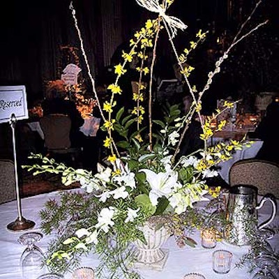 Table centerpieces by Bullfrogs and Butterflies featured greenery interspersed with white lilies and orchids and pussywillow splayed above the table. Long vines with small yellow flowers reached toward the ceiling and were tied together with raffia at the tips.
