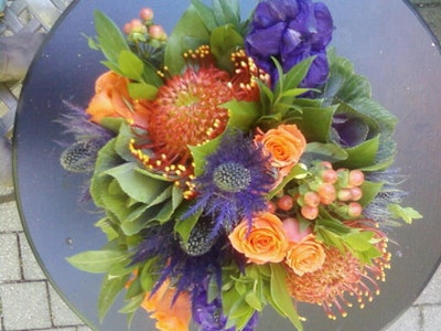 Fisher creates arrangements with seasonal flowers like ornamental cabbage, pincushion, orange sweetheart spray, roses, and purple thistle.