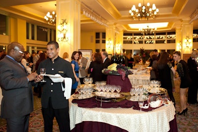 A table decorated with wine bottles and grapes served as a wineglass station for guests.