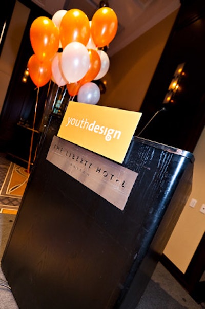 A lectern at the front of the Liberty Hotel's ballroom included Youth Design branding and on-theme orange and white balloons.