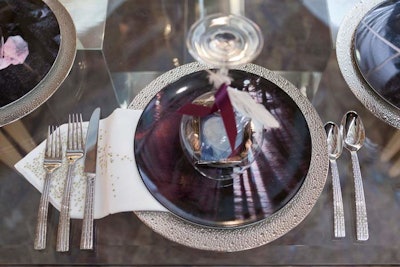 Jeffrey Brooks Interior Design placed small picture frames under overturned goblets. Napkins embroidered with tiny metallic designs completed the look.
