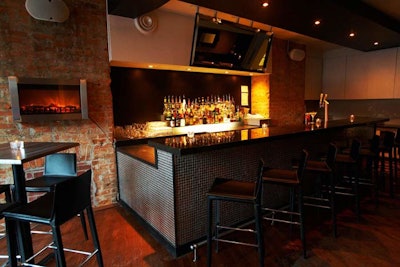 The decor at Boutique Bar blends chic and homey elements, with brick walls, a tiled black bar, and a glass-fronted fireplace.