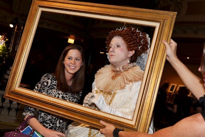 A male performer dressed as Queen Elizabeth posed for photos with guests; staffers held up a golden frame to accent the images.