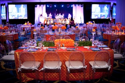 In contrast to the Friday night decor, Blooming Design & Events used bright orange linens on the 29 tables at the Saturday night gala. The ice Chiavari chairs at the round tables were topped with sapphire blue cushions.