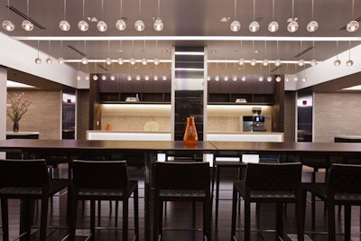 A long high-top table is part of the communal design for the space and sits in the center next to a open kitchen prep area.