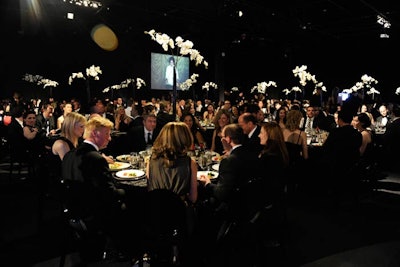 Dimly lit and draped in black, from the walls to the table linens, the dinner space felt intimate despite its size. Tall arrangements of orchids reached above diners, providing the centerpieces for each table.